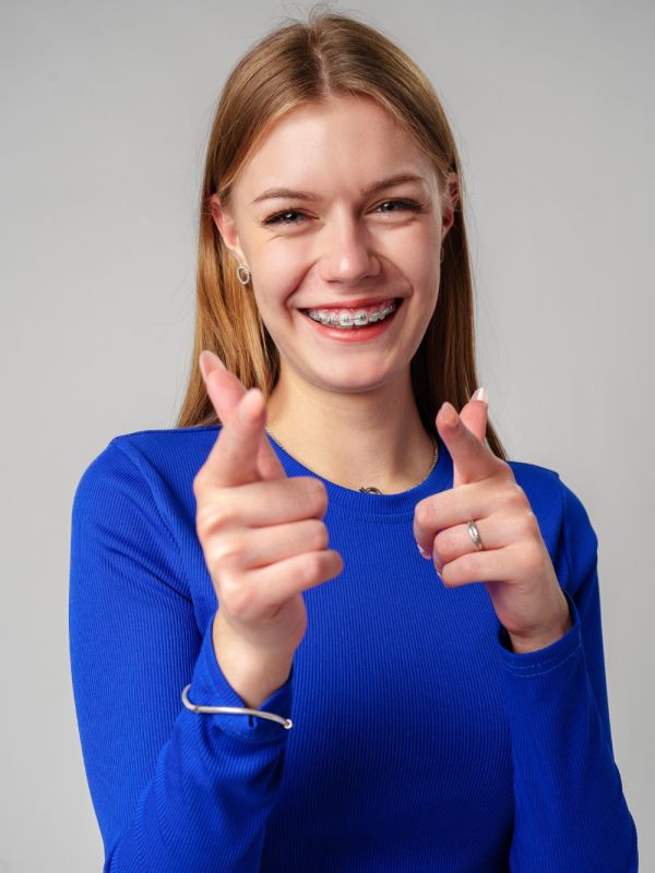 Smiling young woman with braces pointing towards camera in studio