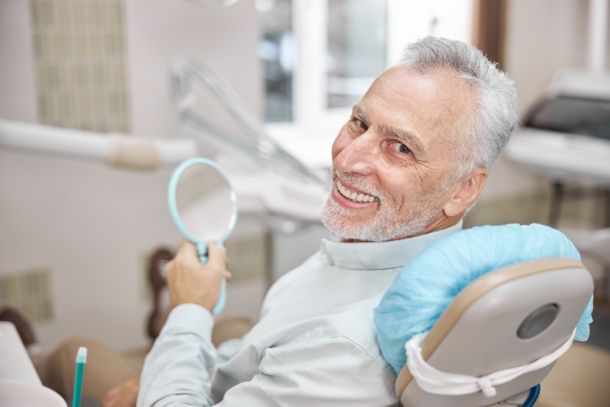 senior man in a dentist chair holding a mirror and smiling